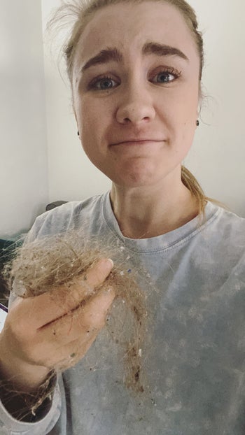 BuzzFeed editor looking deeply disgusted with herself and holding the giant hairball from the floor 