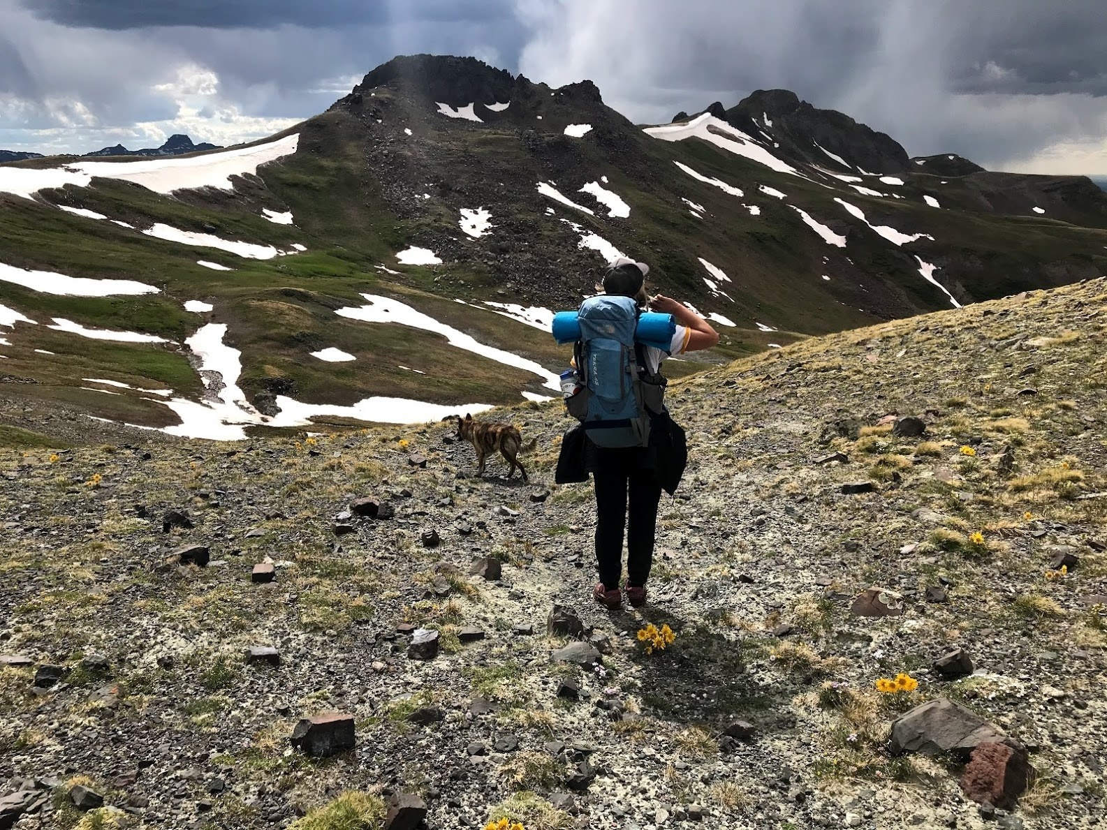 woman wearing a big backpack walking across rocky mountain terrain