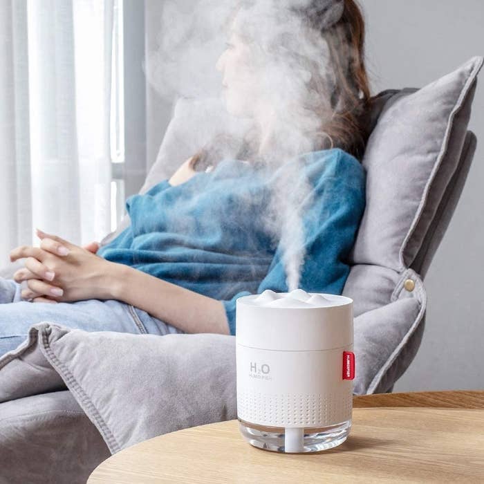 A small humidifier sitting on a side table A person is sitting on a couch beside the table