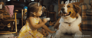A little girl in a sundress attempting to give a dog a cup of tea during tea time. 