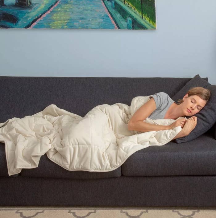 Woman cuddled up with a cream-colored weighted blanket on a gray couch