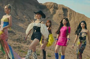 ITZY poses in the desert in sparkly dresses of multiple colors and patterns, high boots, and jewelry 