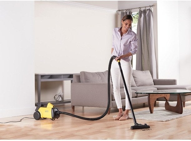 Model using a yellow vacuum with black wheels, hose, and attachment 