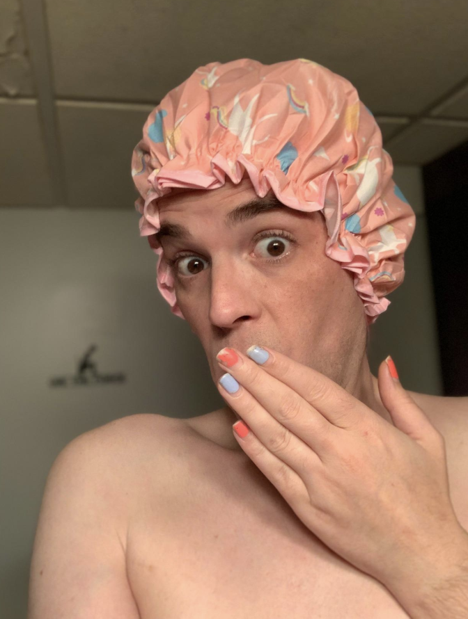 A reviewer with a pink unicorn print shower cap on their head 