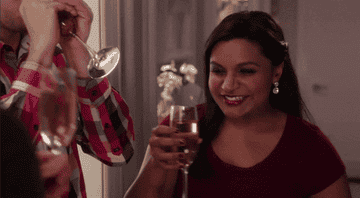 Mindy Kaling laughing and sipping champagne from a flute.