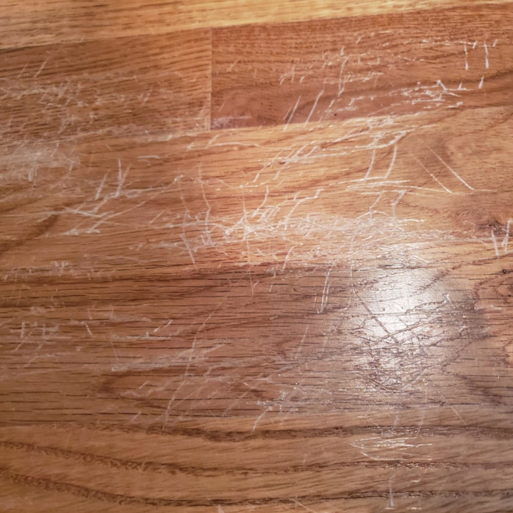 A reviewer's hardwood floor with many scratches made by their child repeatedly jumping on a bed, causing the legs to constantly scratch the floor