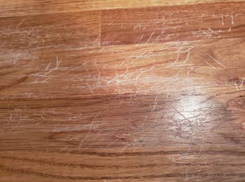 A reviewer's hardwood floor with many scratches made by their child repeatedly jumping on a bed, causing the legs to constantly scratch the floor