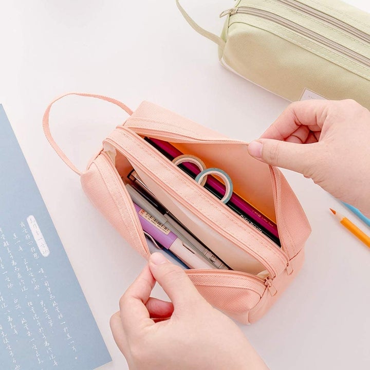 A person opening a canvas pencil case filled with pencils and pens