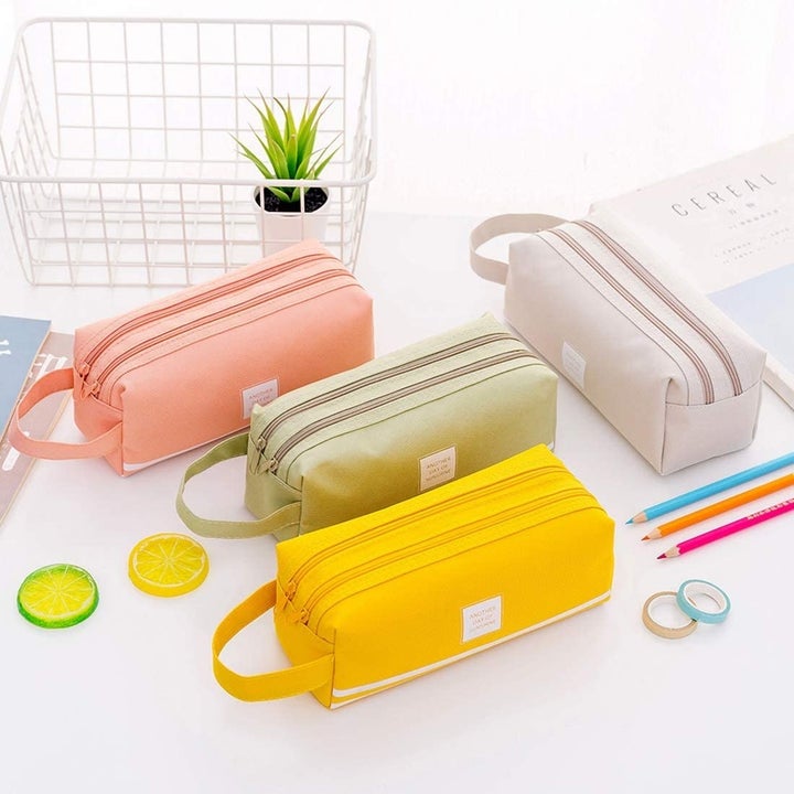 Four canvas pencil cases surrounded by stationery supplies