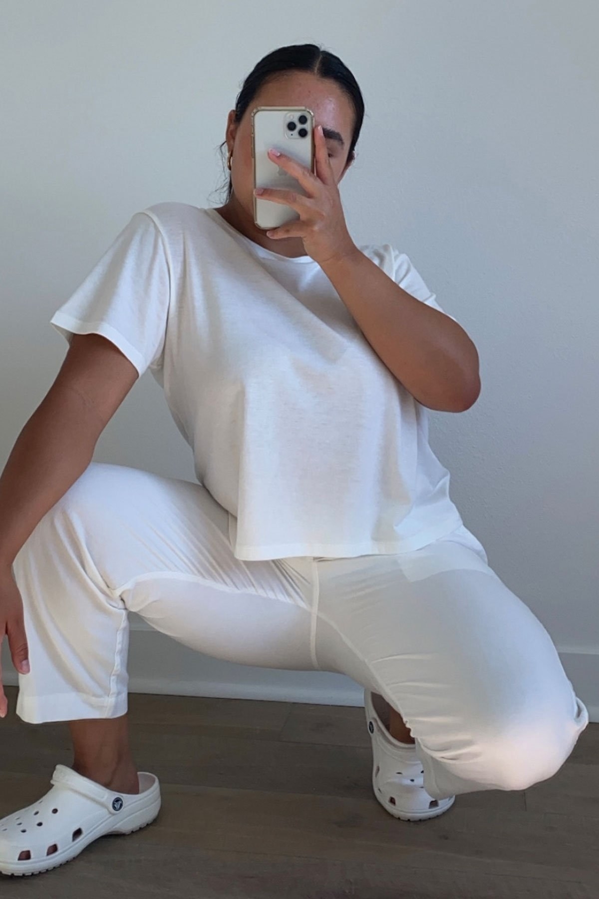 Model wearing the white scoop-neck cropped tee with white pants while taking a mirror selfie