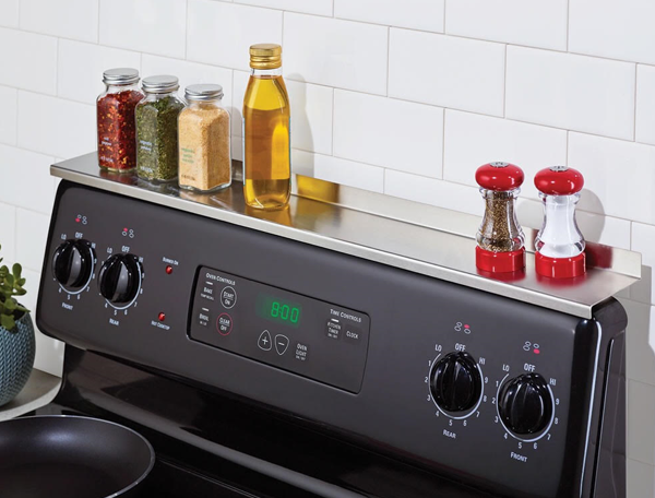 Product photo showing the stainless steel Stove Shelf above a stove with spices, salt and pepper, and olive oil resting on it