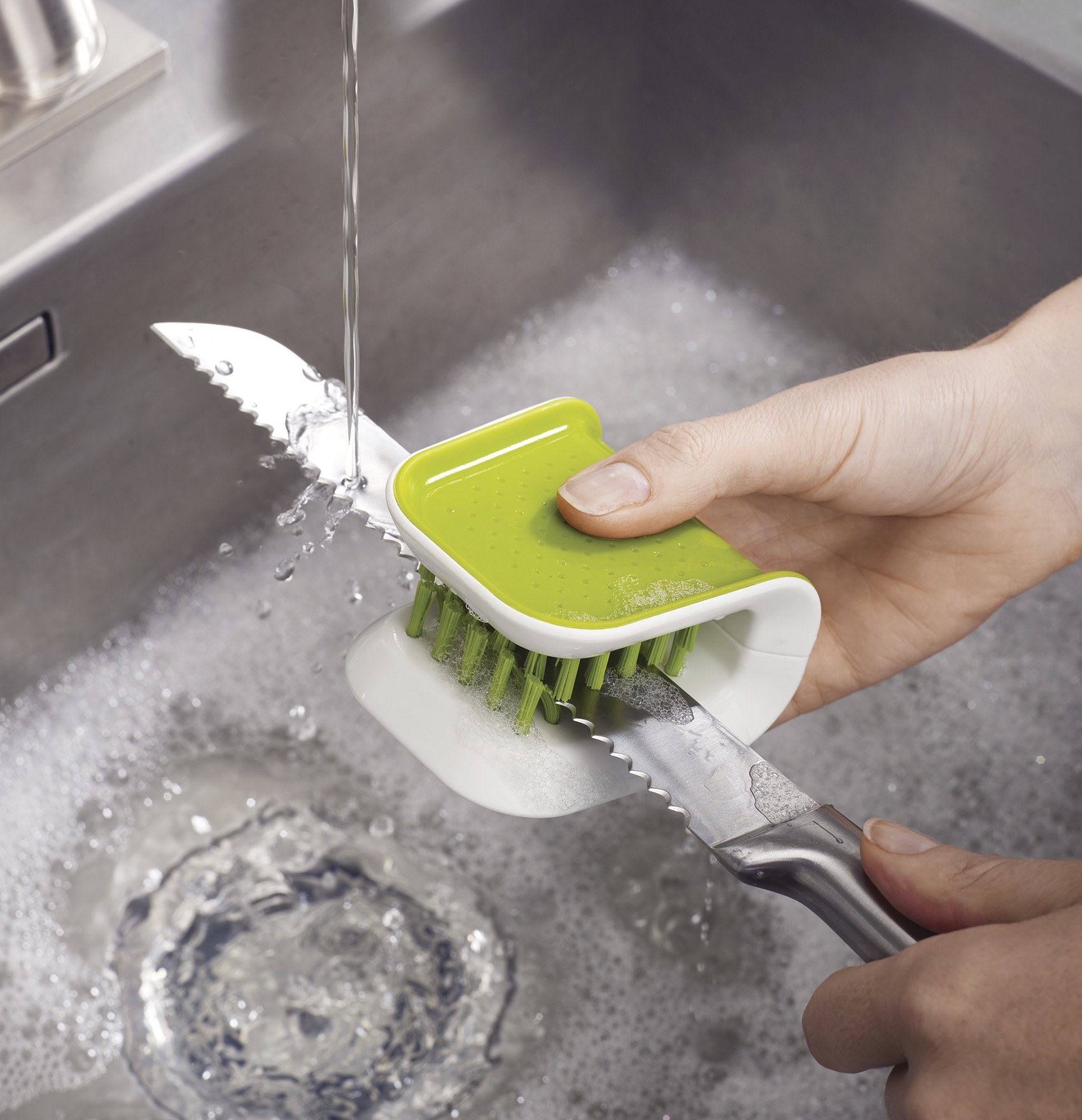 Product photo showing a model using the Joseph Joseph BladeBrush to clean a large kitchen knife
