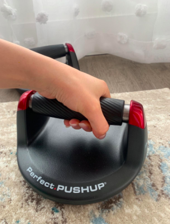 Reviewer holds a black and red push-up bar in their hand on the floor