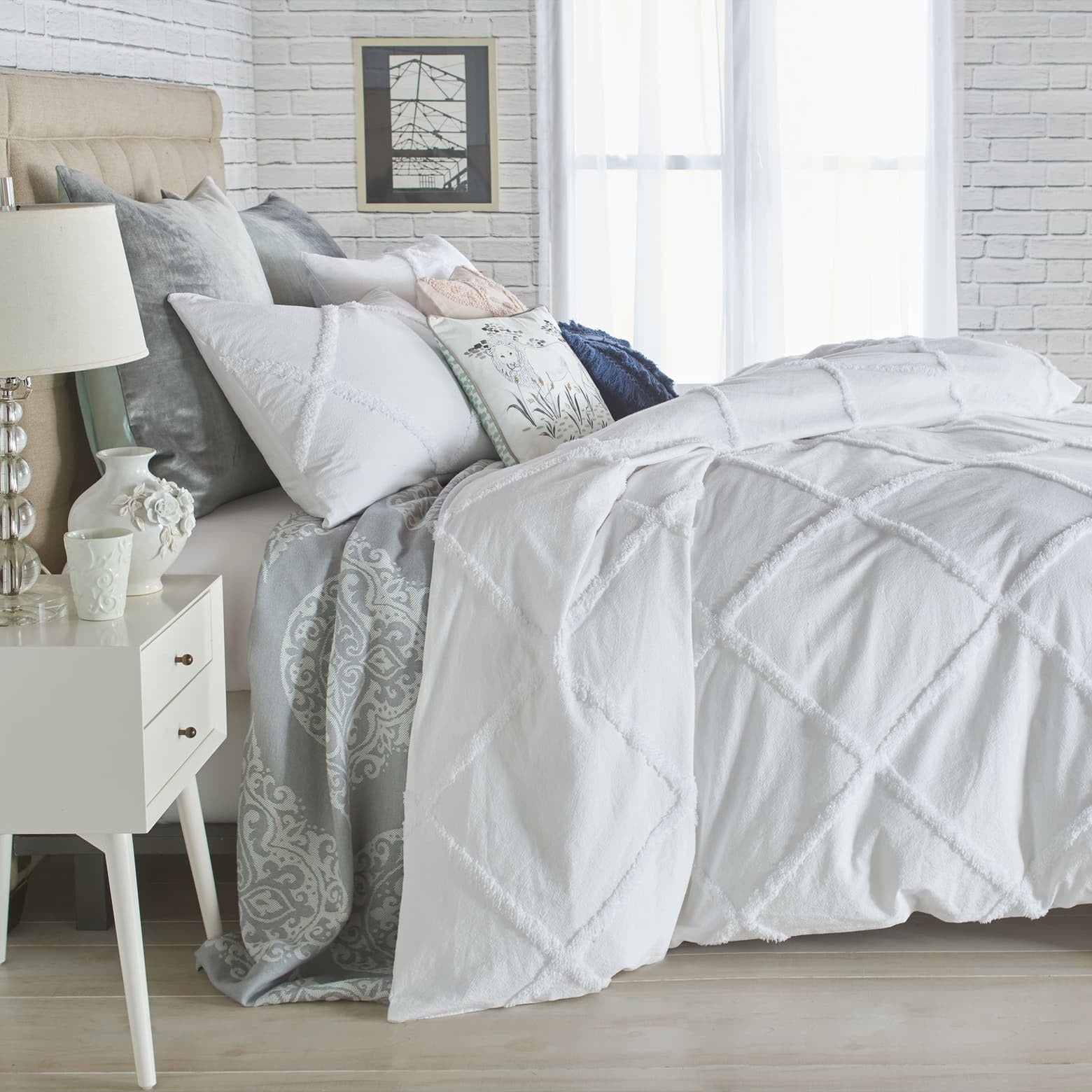 The white lattice duvet cover over a duvet on a bed with assorted pillows on it