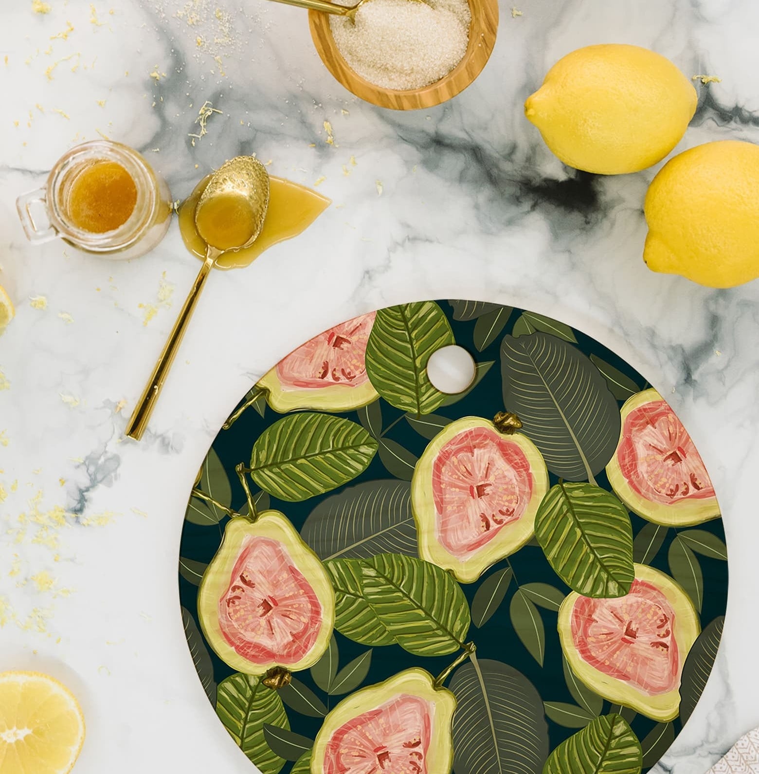 Round cutting board with illustrations of the insides of guavas and green leaves all over