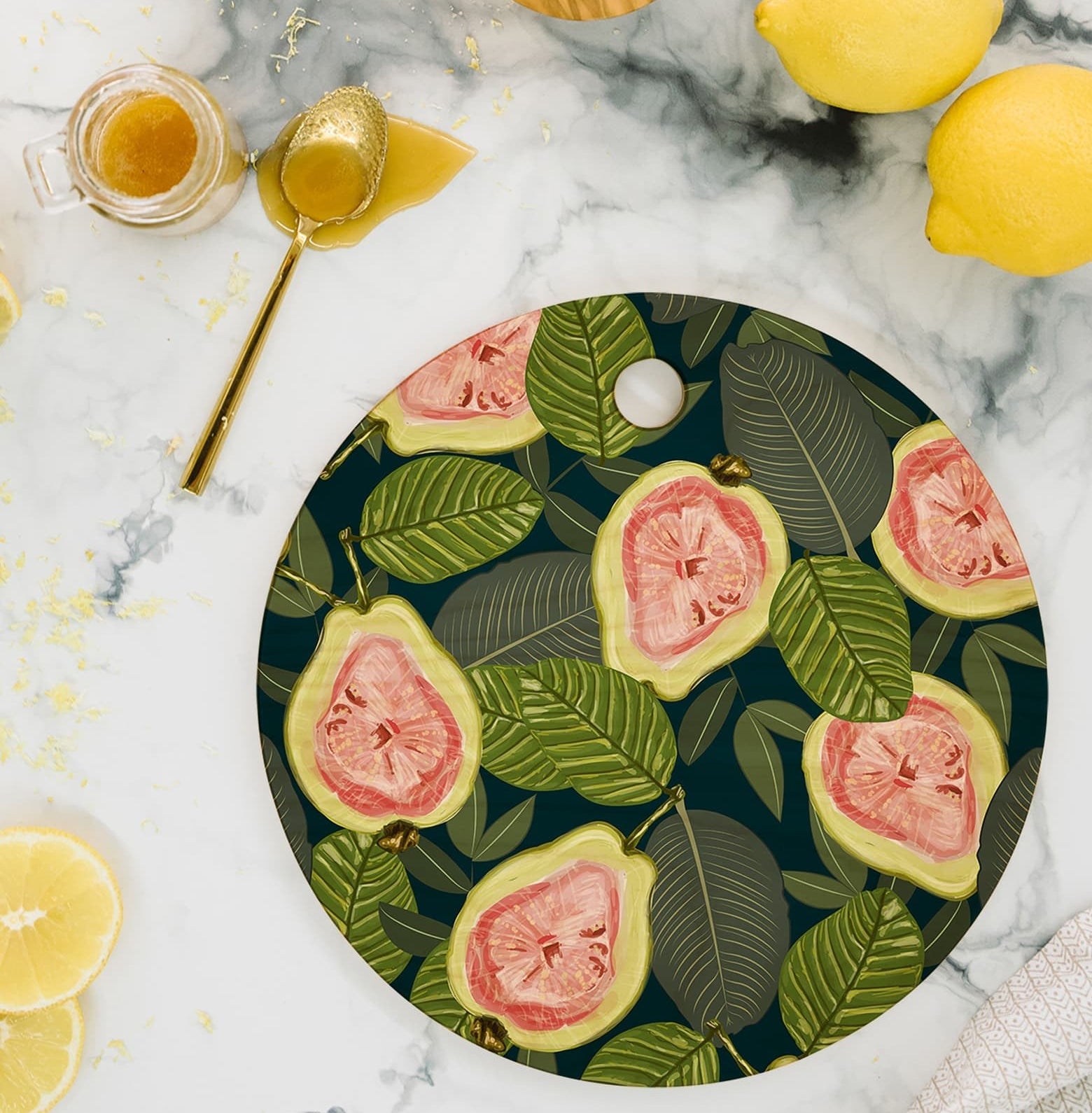 Round cutting board with illustrations of the insides of guavas and green leaves all over