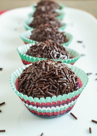 A line up of round brigadeiros in colorful paper cups, covered in sprinkles