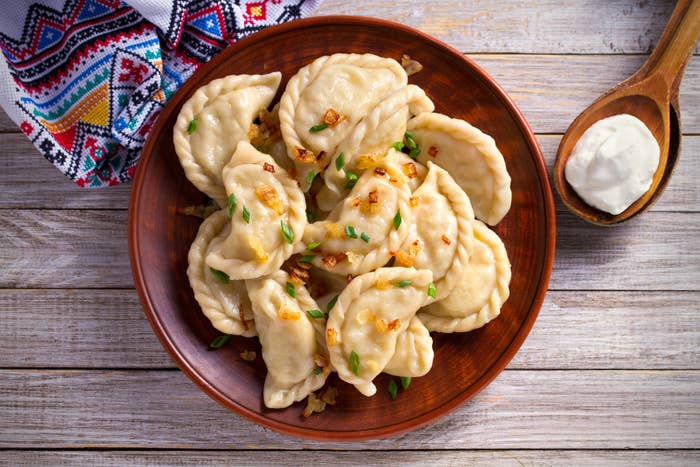 bowl of pierogi dumplings topped with chives and a spoonful of sour cream on the side
