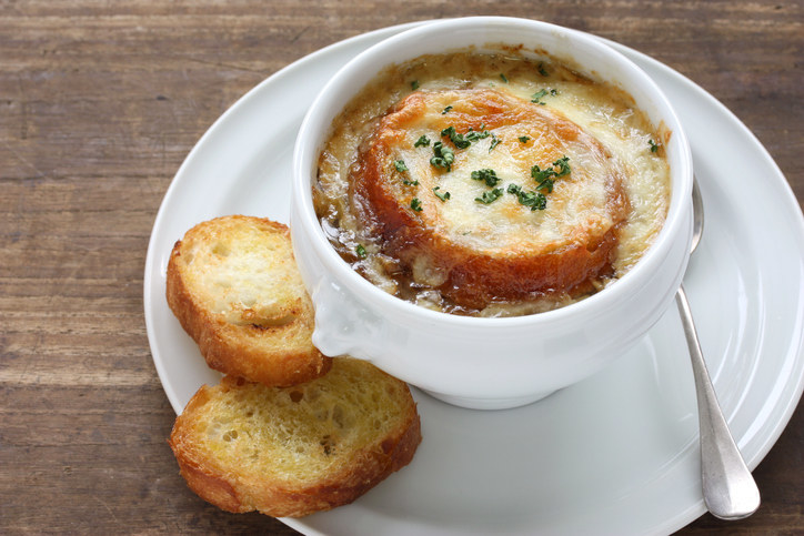 bowl of caramelized onion soup topped with a slice of toasted baguette and melted cheese