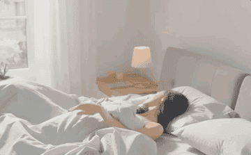 Woman gets out of her bed slowly, facing the sun 