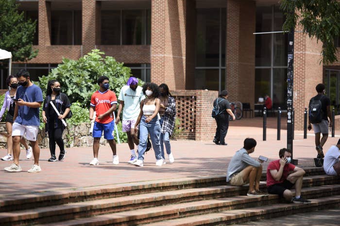 Several students, all wearing masks, walk through the campus of UNC