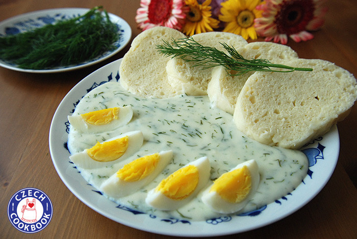 A creamy, dill studded sauce, slices of hard boiled egg, and a soft, dense bread together on a blue and white china plate