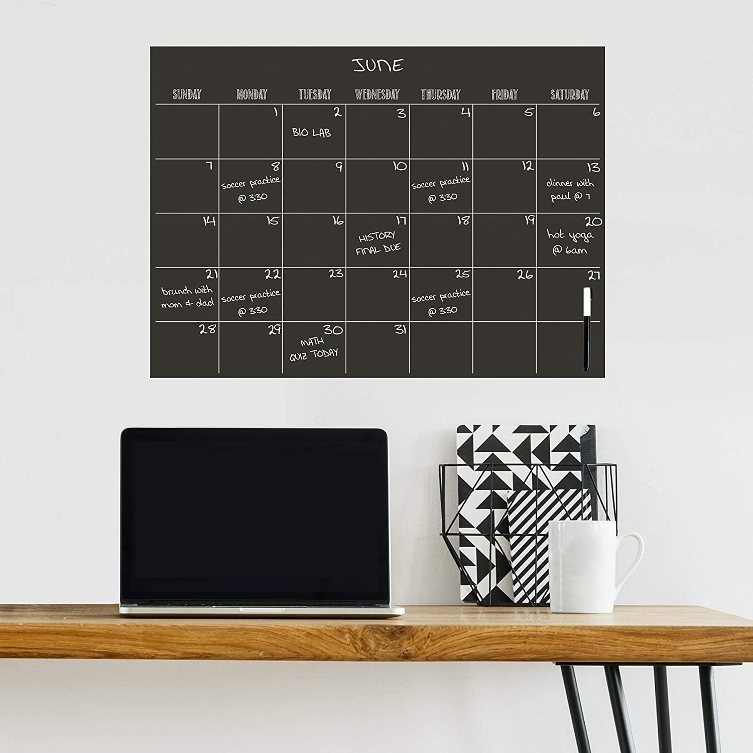 A dry-erase calendar on a wall above a desk