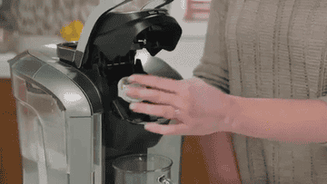 A GIF of a person putting a cleaning K-pod into a Keurig coffee maker