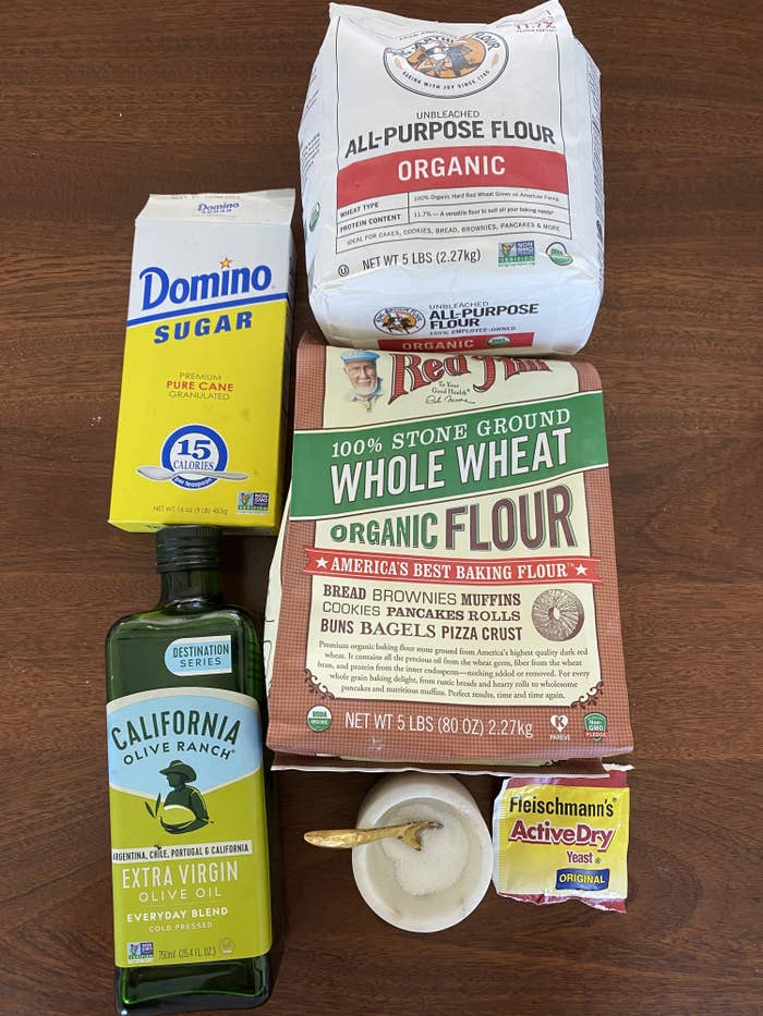 Ingredients for pita -- flours, olive oil, yeast, salt, and sugar -- on a countertop.