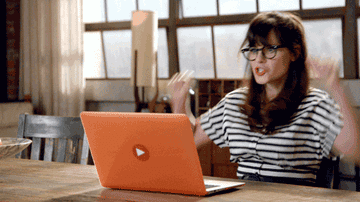 Gif of Zooey Deschanel in the TV show &quot;New Girl&quot; sitting in front of her computer and raising her arms in the air in excitment
