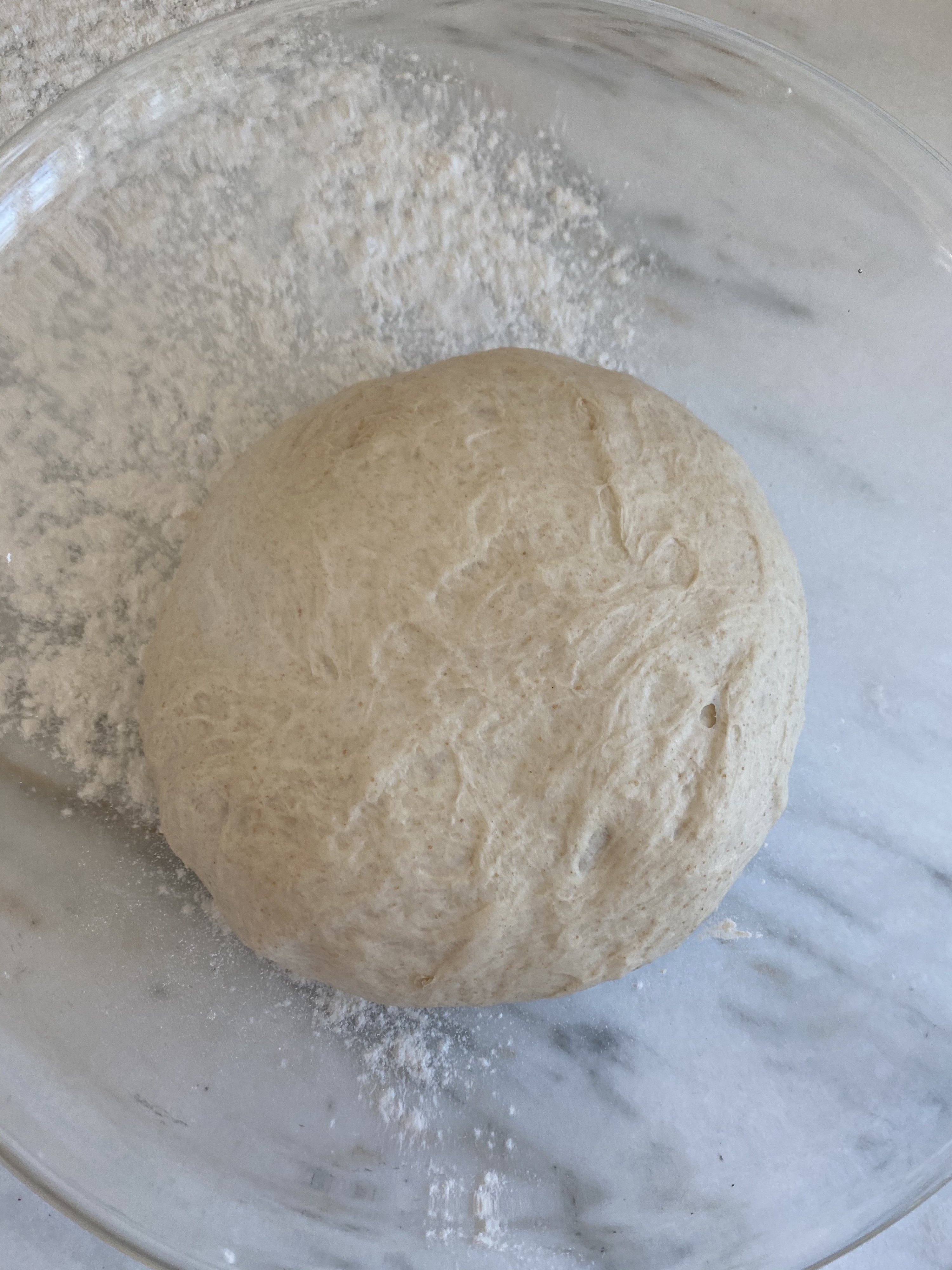 A ball of dough rising in a glass mixing bowl.
