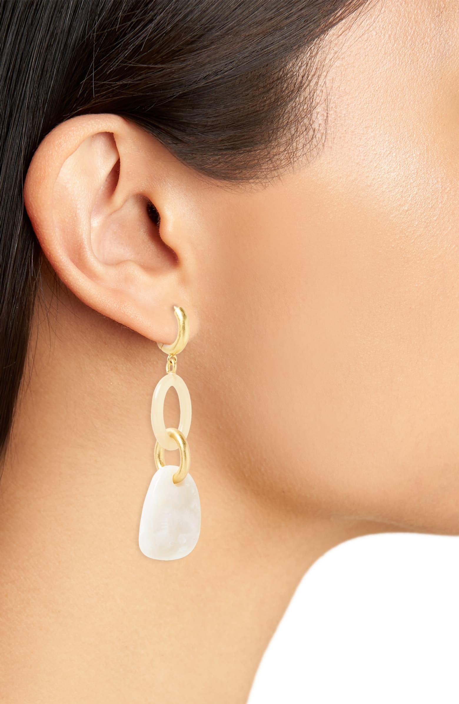 a model wearing the earrings with a gold hoop that connects to a pale pink hoop, connected to another small gold hoop, connected to a white stone