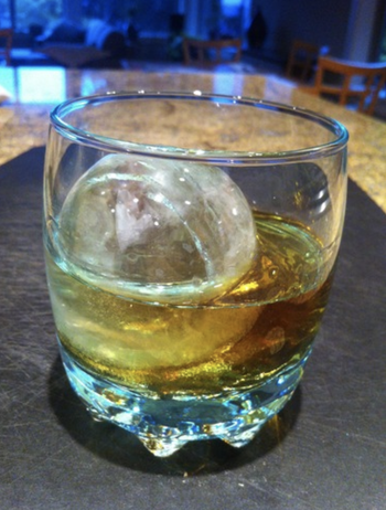 a sphere shaped ice cube in a whiskey glass