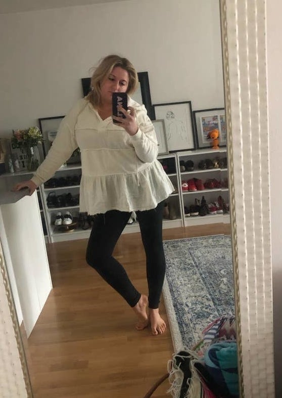 BuzzFeed writer Elena Garcia wearing the black leggings with a white blouse while taking a mirror selife