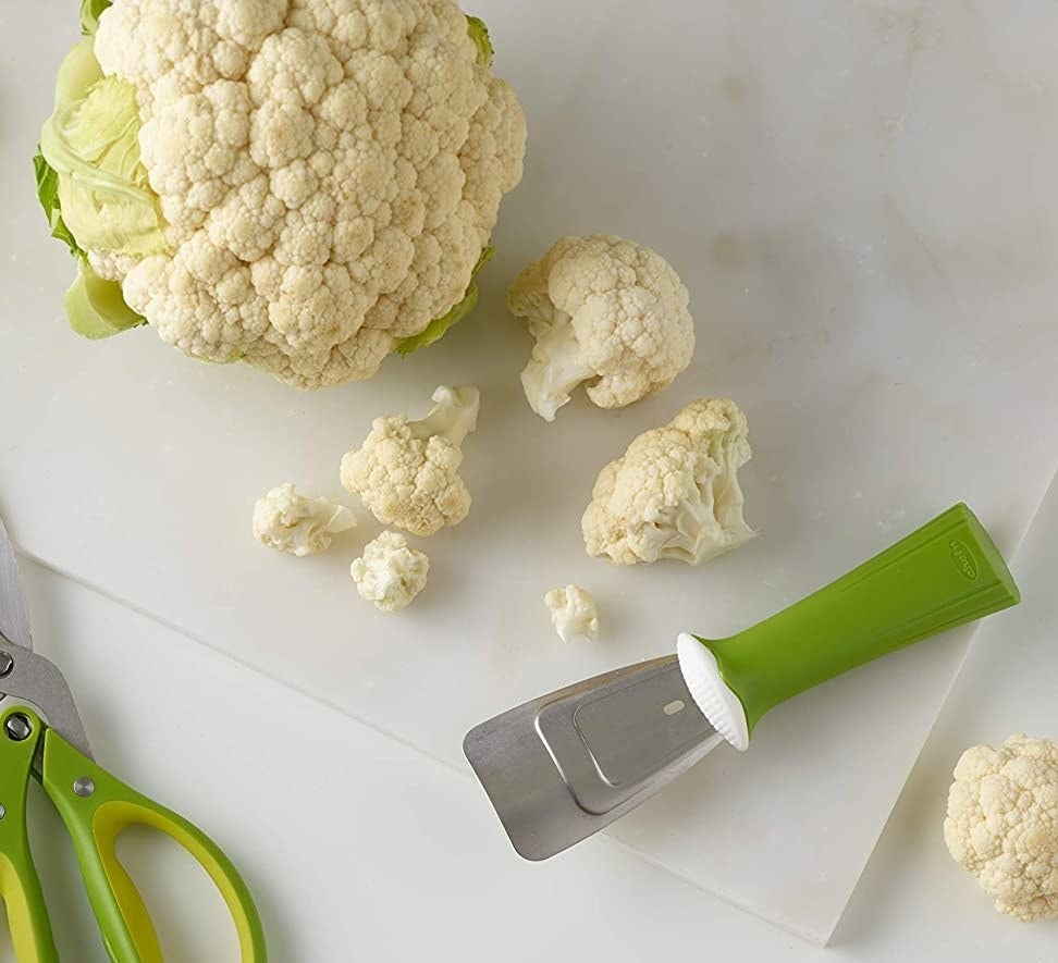 The cauliflower tool next to chopped up florets of cauliflower and a head of cauliflower