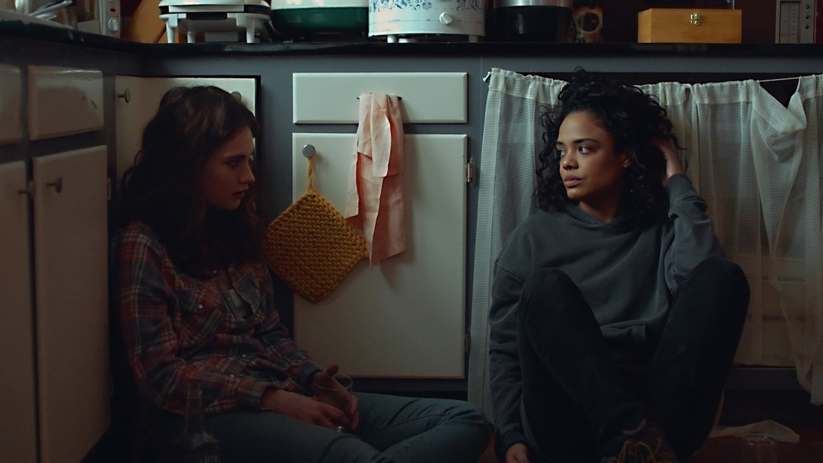 Tessa Thompson and Lily James sit on the floor of a kitchen and look at one another
