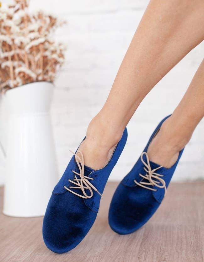 A model wearing the round toe, royal blue flats with tan laces