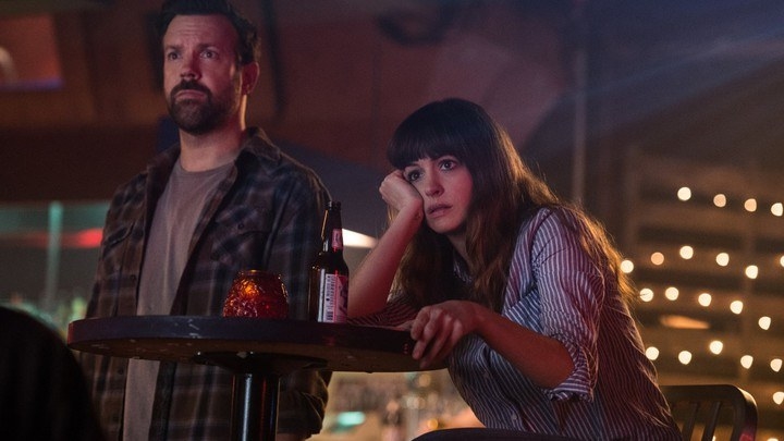 Jason Sudeikis and Anne Hathaway look bored at their small table at a bar