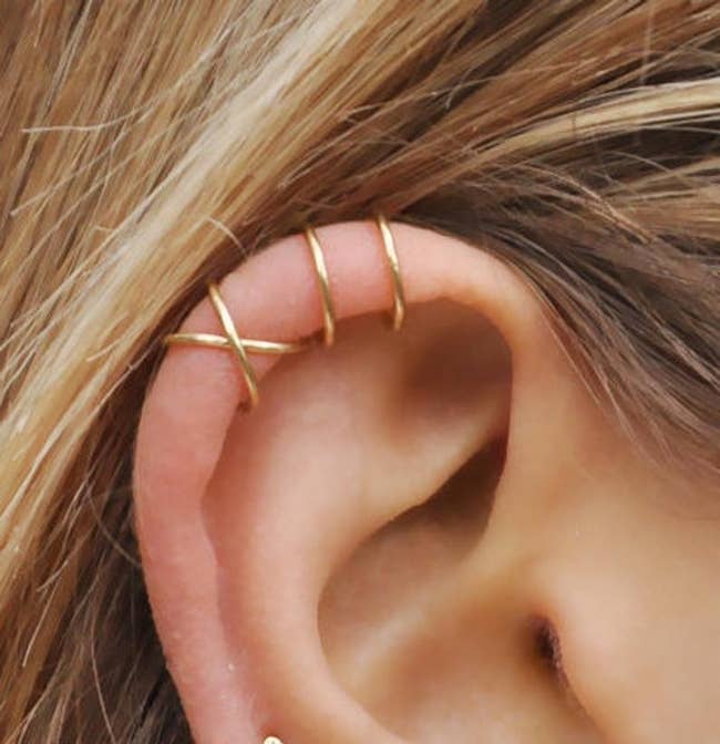 A model's earlobe with both styles of cuff — the crisscross one and the two bar one  — in gold
