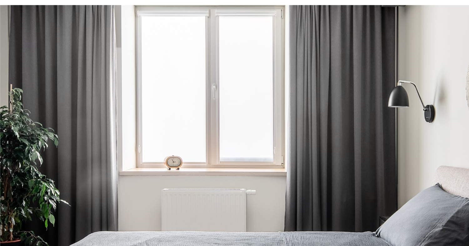 Curtains hanging in a bedroom with a window letting in sunlight