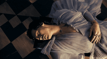 Harry lying on the floor wearing a poofy sheer top in a music video