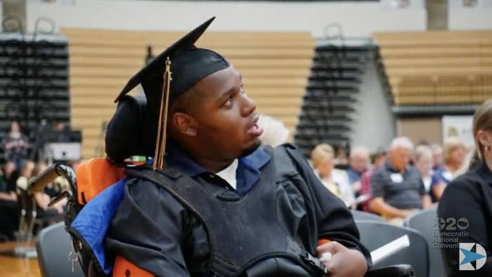 DeAndre Knox wears a graduation cap and gown and sits in a wheelchair in a school gym