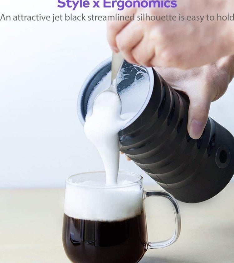 A person pouring foamy milk from the frother into a mug of coffee