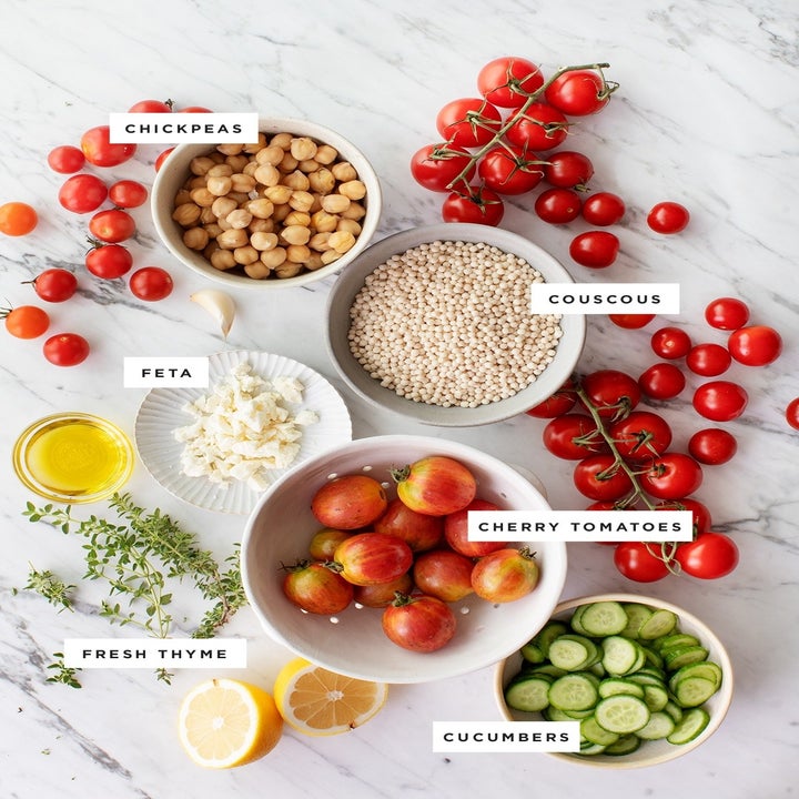 Labeled ingredients on a countertop including cucumbers, cherry tomatoes, chickpeas, couscous, thyme, and lemon.