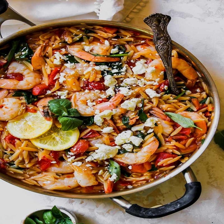 A pot full of orzo, tomatoes, shrimp, and herbs topped with crumbled feta.