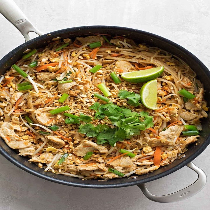 A skillet with rice noodles, shredded carrots, crushed peanuts, and fresh herbs in peanut sauce.