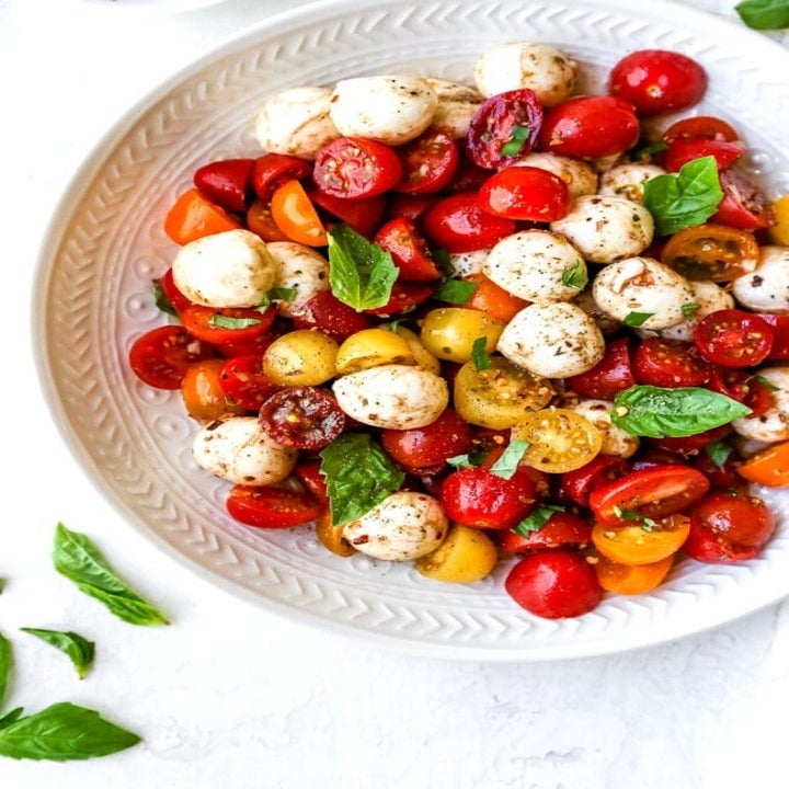 A bowl of multi-colored cherry tomatoes, mozzarella balls, and basil.