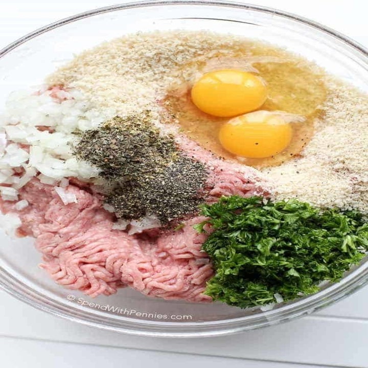 Eggs, bread crumbs, onion, herbs, and ground turkey in a mixing bowl to make meatballs.