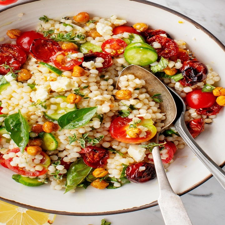 A bowl of couscous with sliced cherry tomatoes, cucumbers, chickpeas, and herbs.