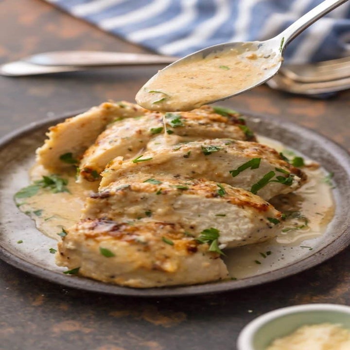 A sliced piece of baked chicken topped with Caesar sauce on a plate.